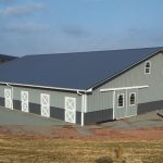 large horse shelter building with gray and green siding, along with a dark-colored roof